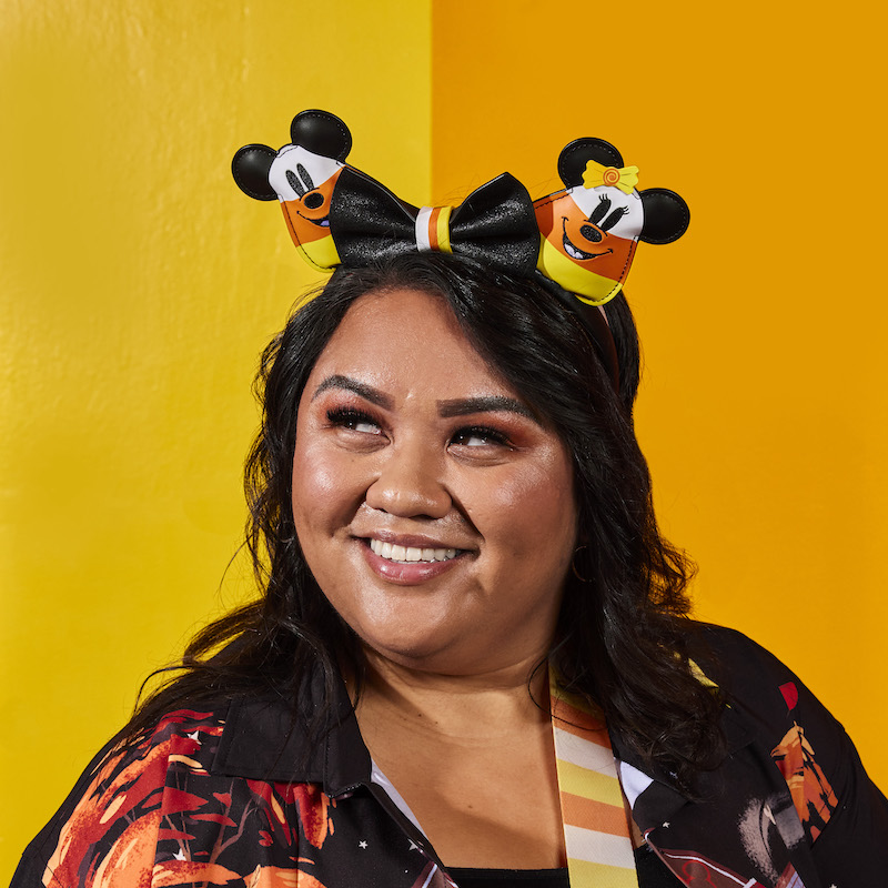 Woman wearing the Mickey and Minnie Mouse Candy Corn Ear Headband, featuring Mickey and Minnie Mouse as candy corn with a removable black bow in the center of the headband. 